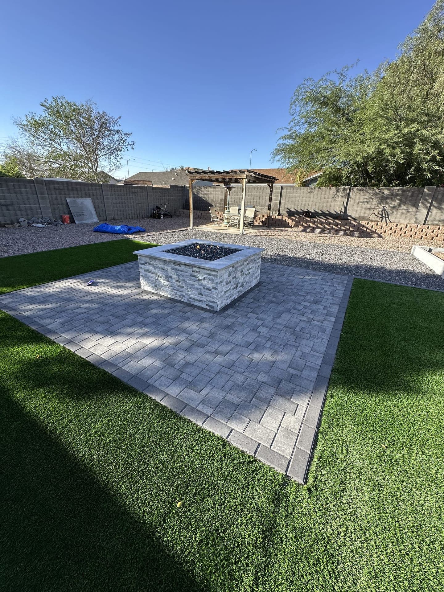 Paver patio with stone fire pit surrounded by artificial turf in San Tan Valley, AZ